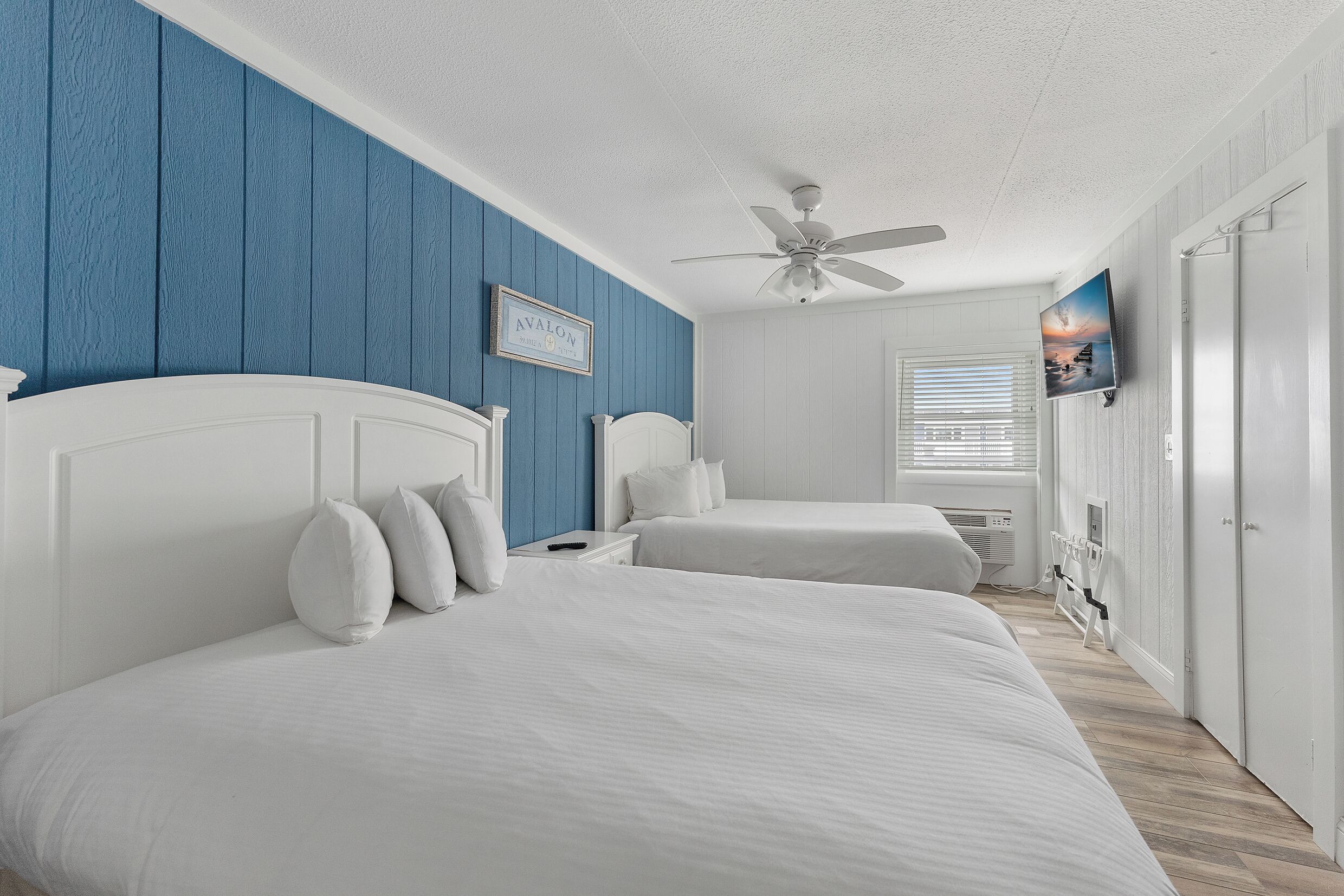 A bedroom with two beds, a ceiling fan, a TV, and a window with blinds.