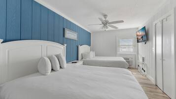 A bedroom with two beds, a ceiling fan, a TV, and a window with blinds.