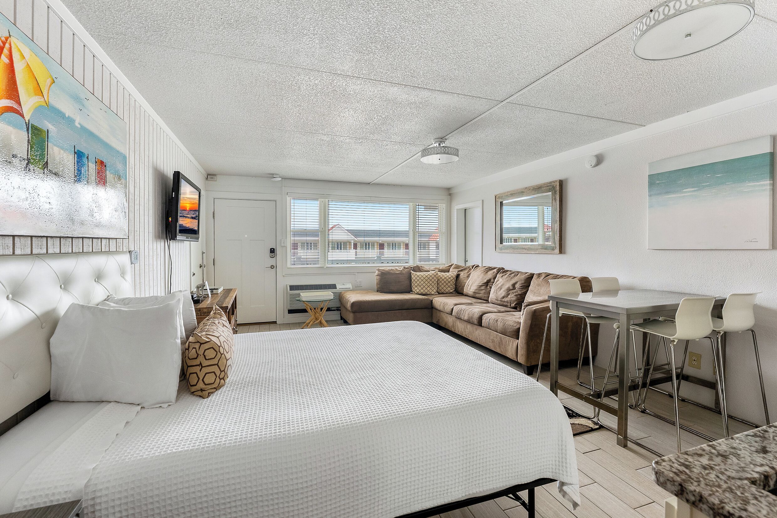 Een moderne hotelkamer met een groot bed, een bank, een eettafel met stoelen en een aan de muur bevestigde televisie.
