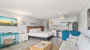 Une pièce compacte et bien éclairée, comprenant un lit, un canapé, un coin repas et une kitchenette.
