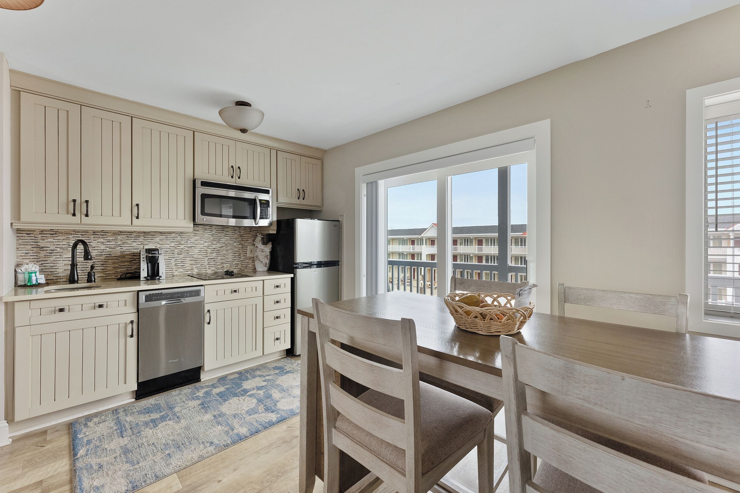 A modern kitchen with beige cabinetry, stainless steel appliances, and a large window offering a view of the city.