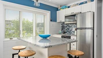 A modern kitchen with a large island, stainless steel appliances, and a view of greenery through the window.