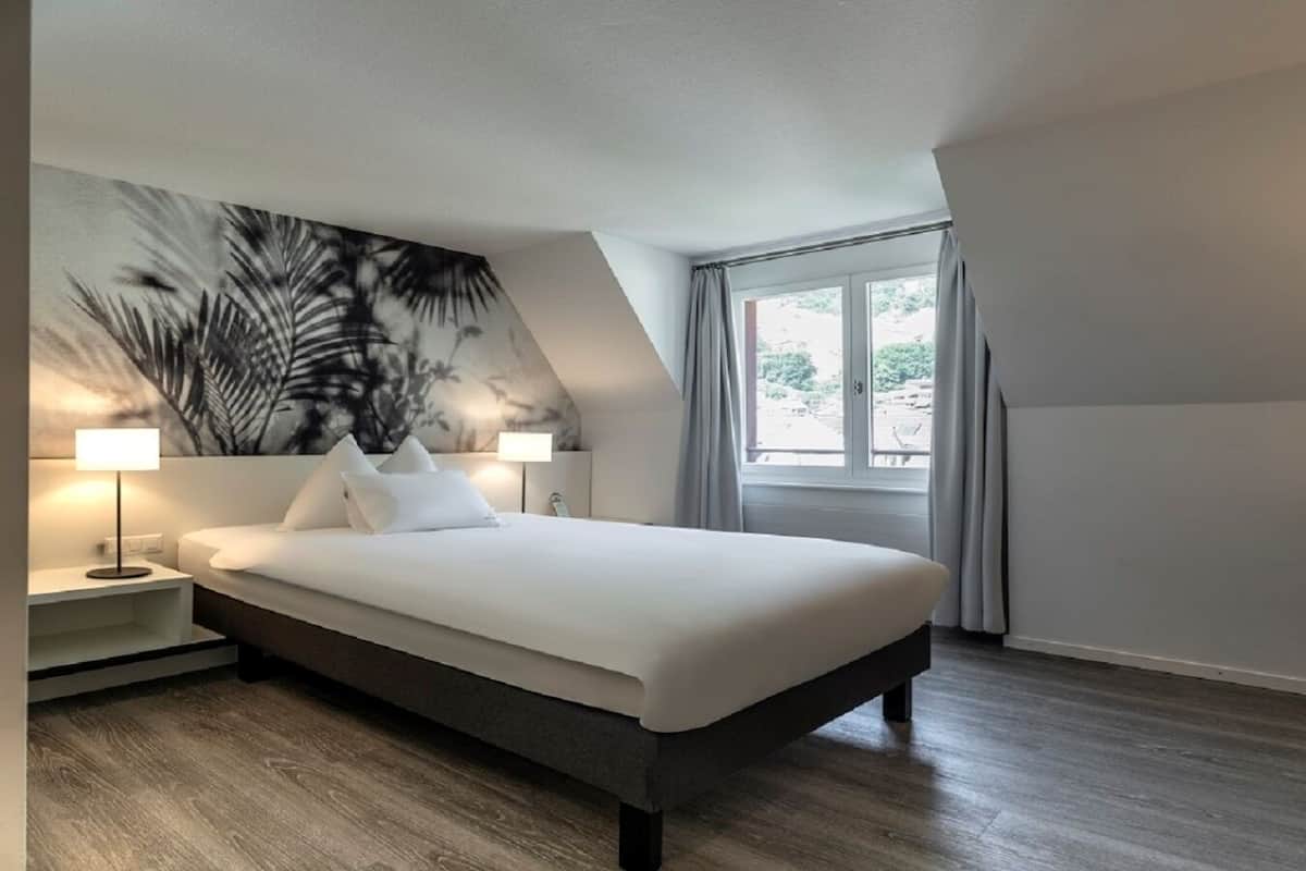 Un dormitorio moderno con una cama grande, dos lámparas de noche, un mural en la pared y un amplio ventanal con cortinas.
