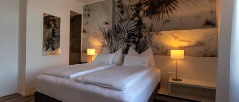 A modern hotel room with a large bed, two bedside tables, and a wall mural.