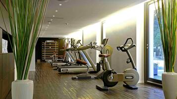 A gym with various exercise machines, a wooden floor, and large windows.