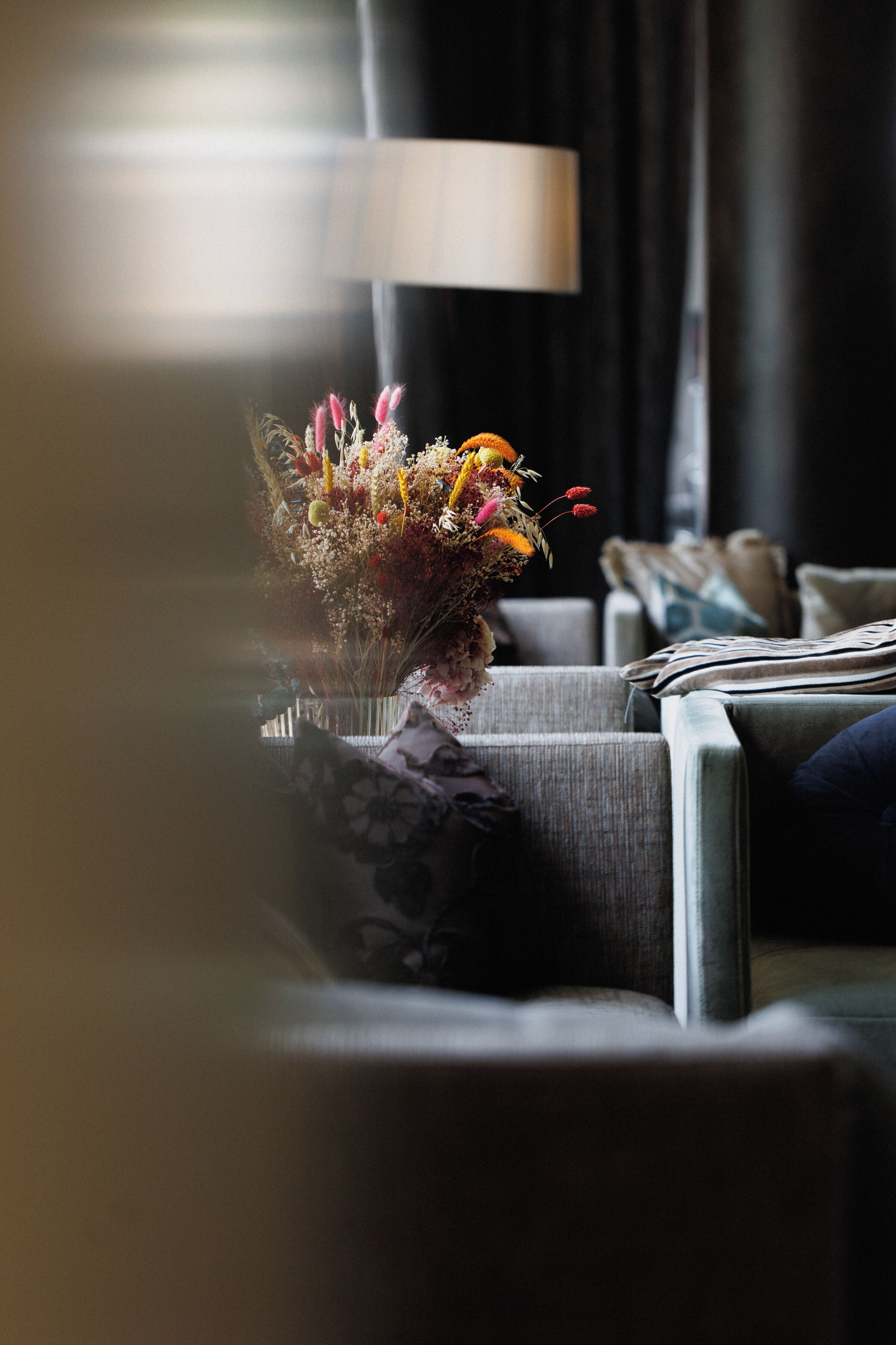 A living room with a sofa, a lamp, and a floral arrangement on the side table.