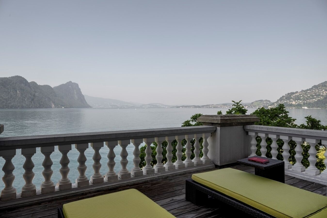 Un balcon avec vue sur un plan d’eau, une terrasse en bois et deux coins salons agrémentés de coussins verts.