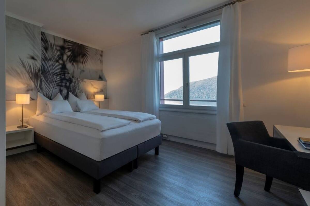 Una habitación de hotel moderna con una cama grande, mesitas de noche, un escritorio y una ventana con cortinas.
