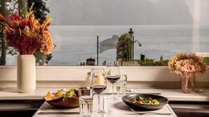Una mesa de comedor con una vela, copas de vino y un tazón de ensalada junto a una ventana con vista a un lago.