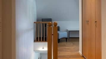 Un pasillo estrecho con piso de madera, una escalera de madera con barandilla y una pequeña zona de estar con mesa y sillas.