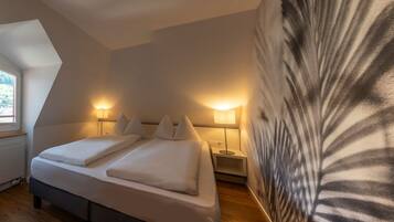 A bedroom with a bed, two bedside tables, a nightstand, a window, and a wall with a leaf pattern.