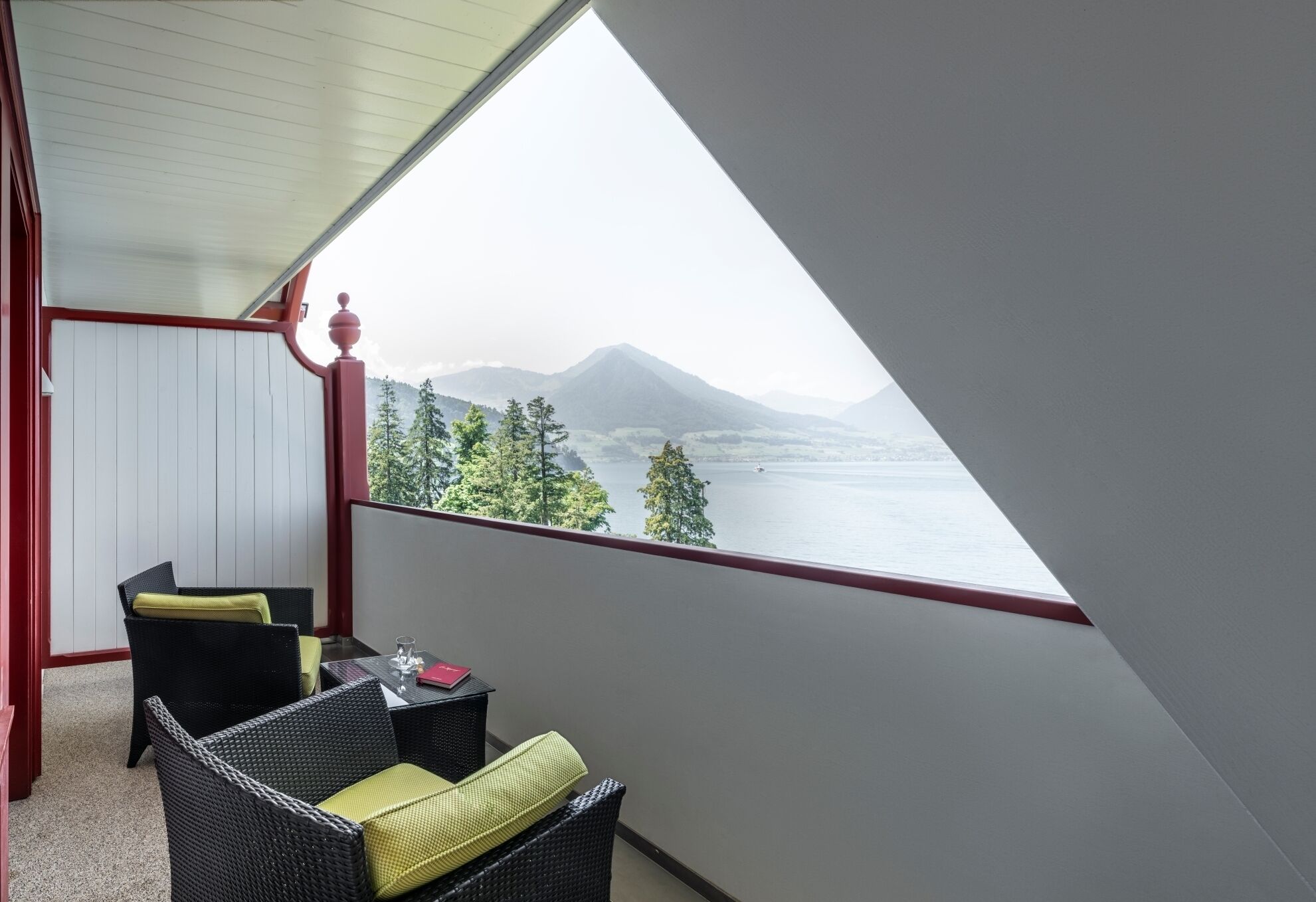 Un balcón con vista a un lago y montañas, amueblado con sillones de mimbre y una mesita.