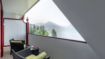 Un balcón con vista a un lago y montañas, amueblado con sillones de mimbre y una mesita.