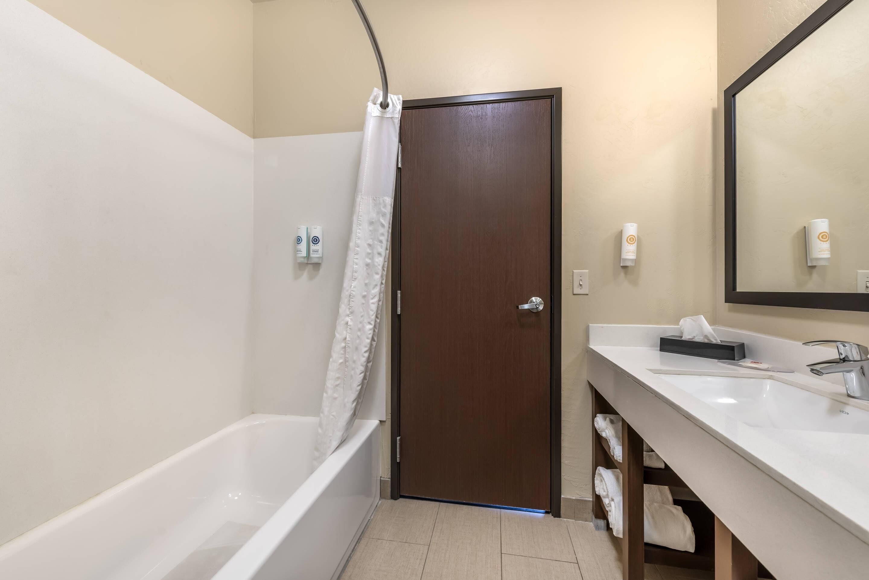 Une salle de bain avec une baignoire, un rideau de douche, une porte en bois, un lavabo avec un miroir et un porte-serviettes.