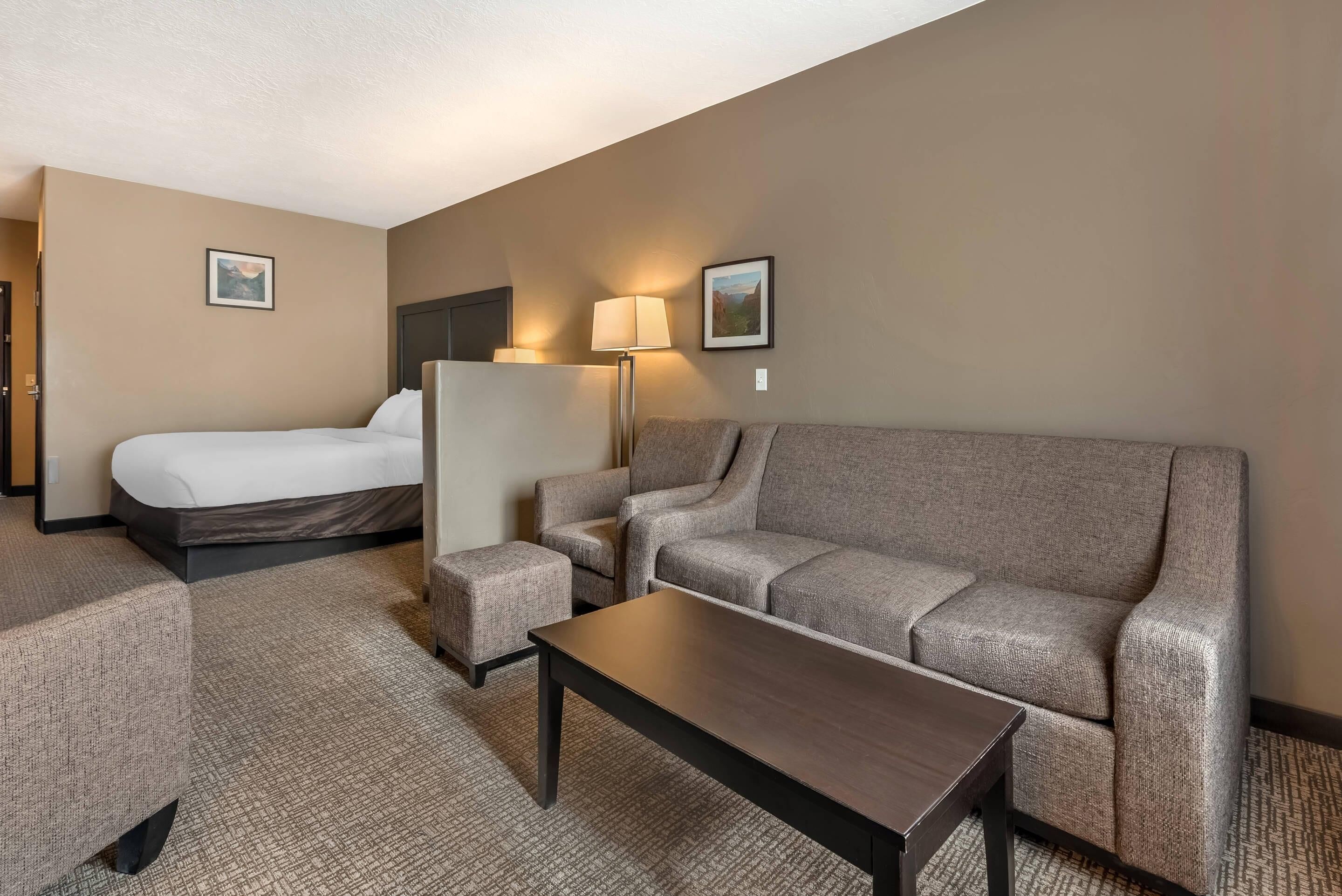 A hotel room with a bed, a sofa, a small table, and two lamps.