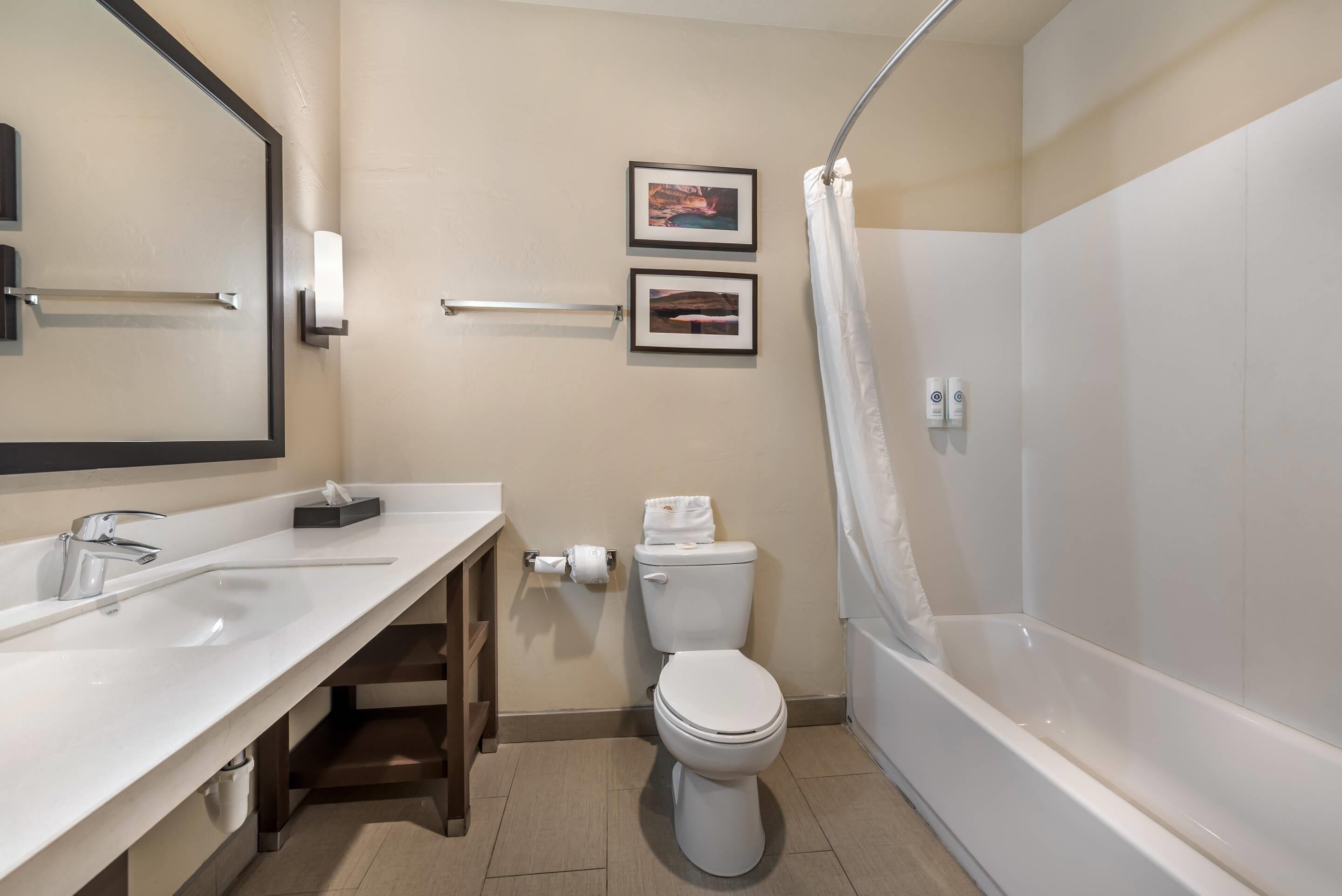 A modern bathroom with a white sink, toilet, and bathtub. There are two framed pictures on the wall and a towel rack.