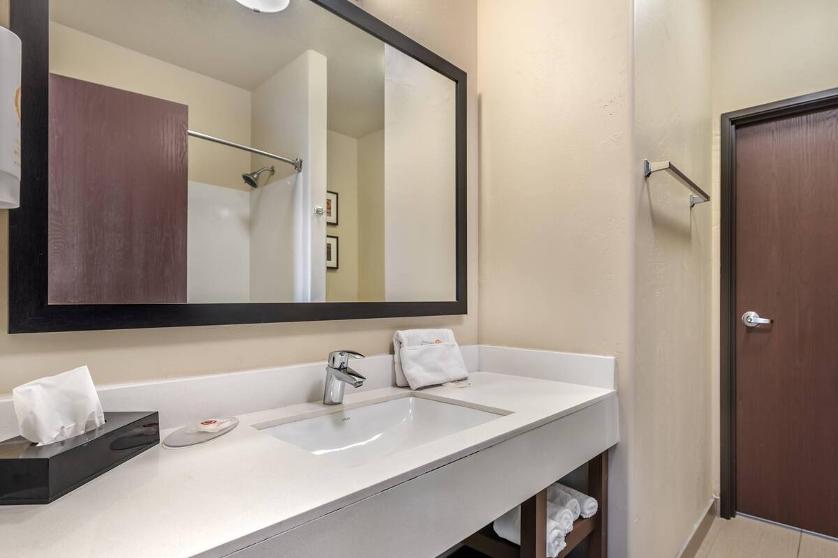 Un baño con lavamanos blanco, un espejo grande, toallero y una puerta.