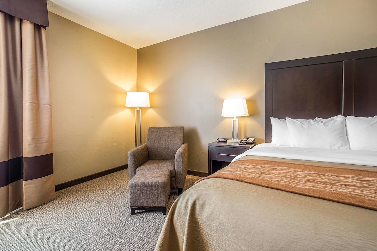 Una habitación de hotel con una cama, una silla, una mesita de noche y dos lámparas.