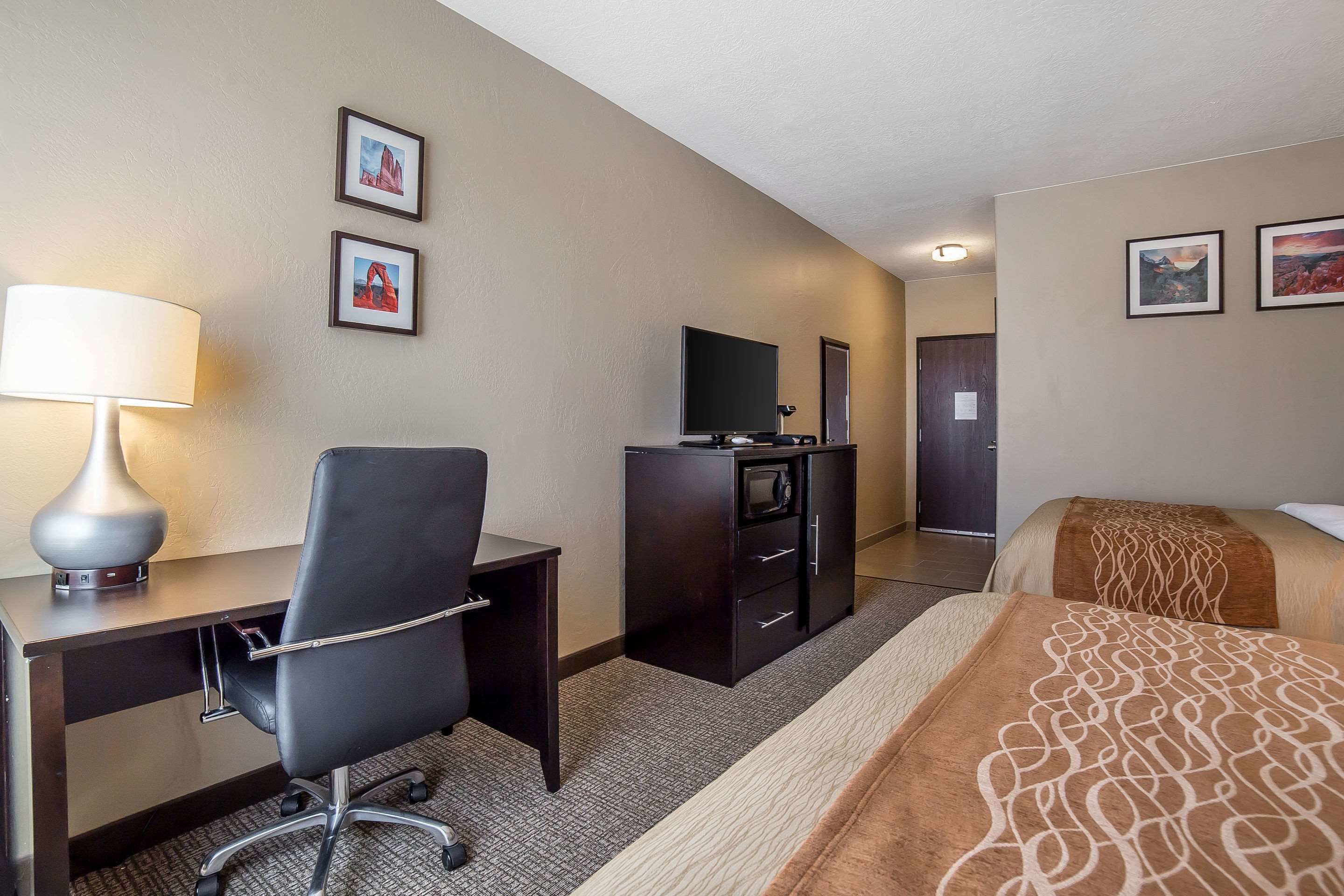 A hotel room with a desk, chair, television, and a bed with a patterned blanket.