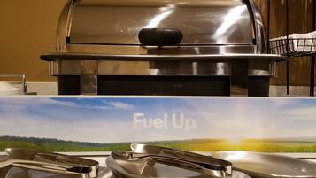 Ein Edelstahlgrill mit Deckel, einer Metallwanne und einem Metallspatel auf einer Arbeitsplatte.