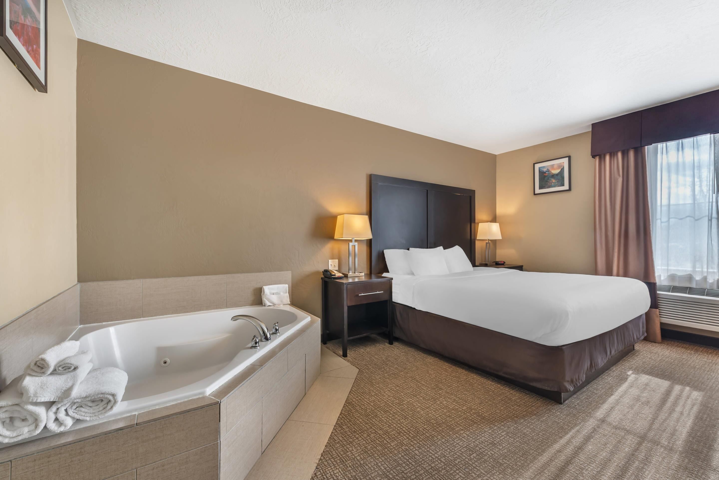 Habitación de hotel con una cama grande, un baño independiente con bañera y una ventana con cortinas.