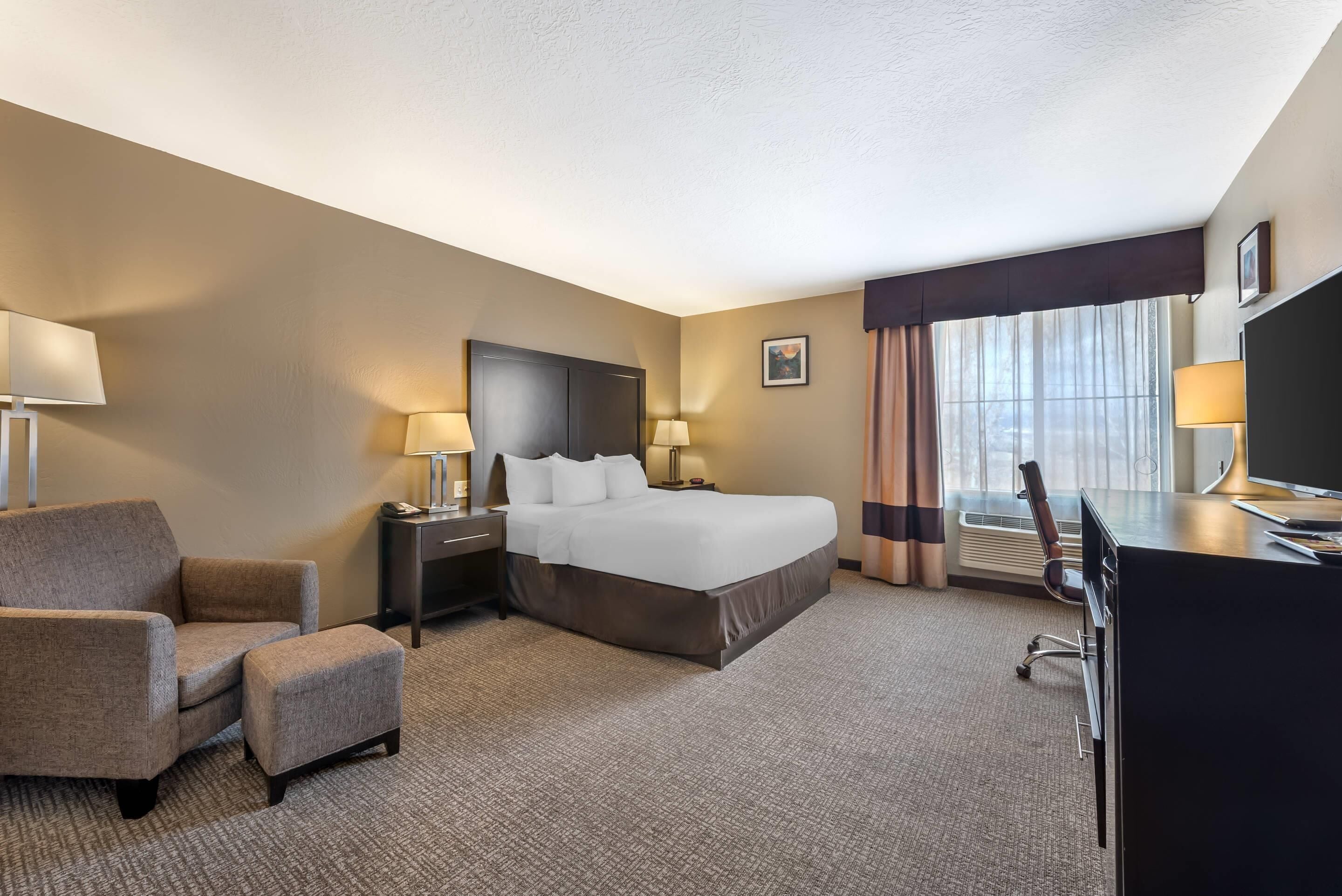 A hotel room with a bed, a desk, a chair, and a TV.