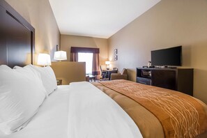 A hotel room with a large bed, a desk with a chair, a television, and a window with curtains.