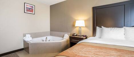 Ein Hotelzimmer mit einem großen Bett, einer separaten Badewanne, einem Nachttisch mit Lampe sowie einem gerahmten Bild an der Wand.