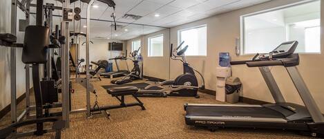 A gym with cardio machines, weightlifting equipment, and a mirrored wall.