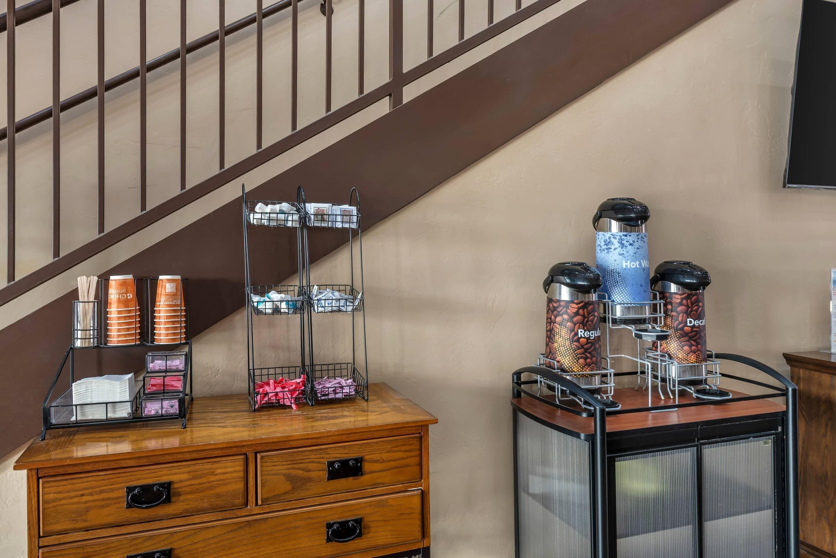 A hotel room with a wooden dresser, a coffee station with dispensers, and a staircase.