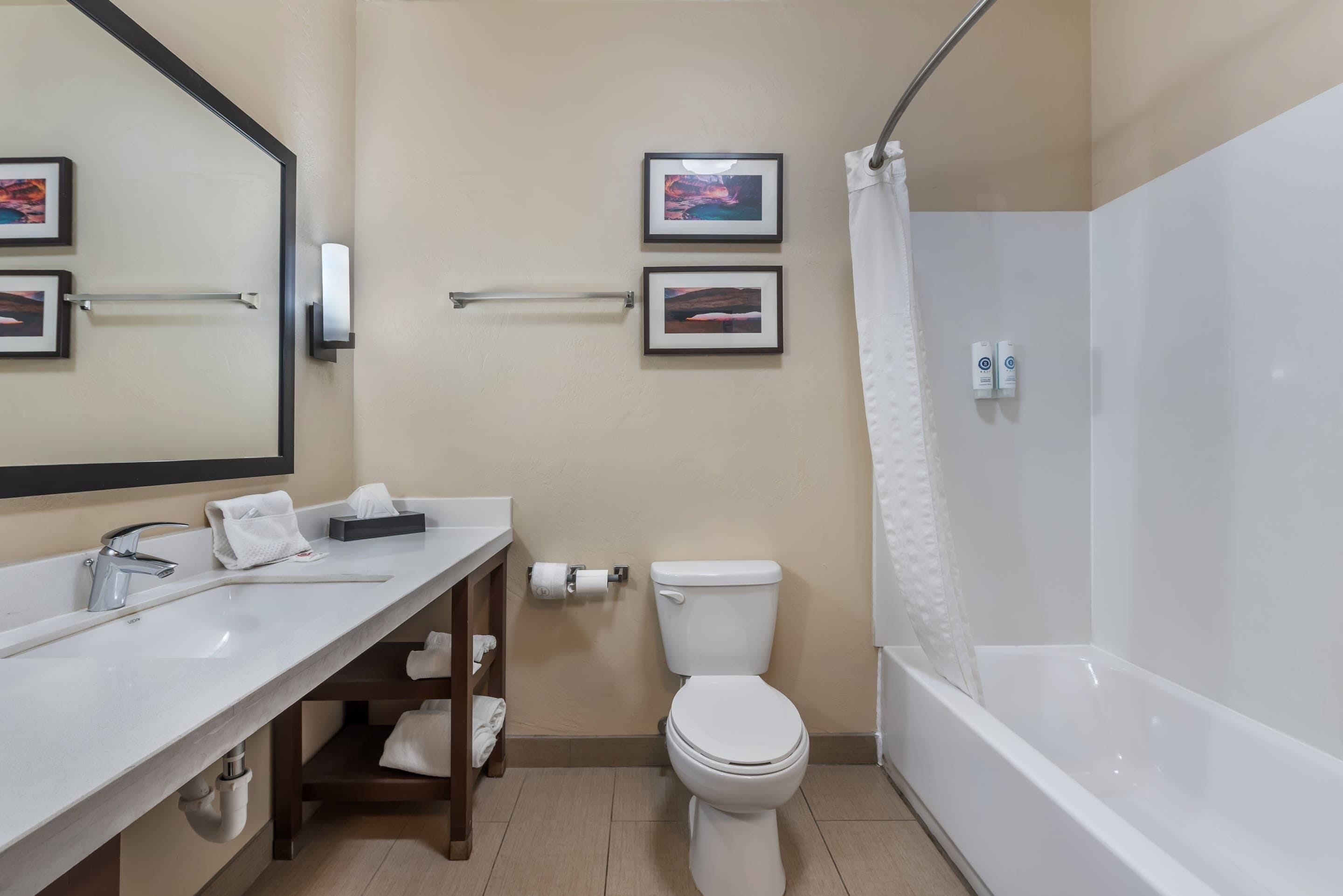 A modern bathroom with a white sink, toilet, and bathtub. There are two framed pictures on the wall, a towel rack, and a hand dryer.