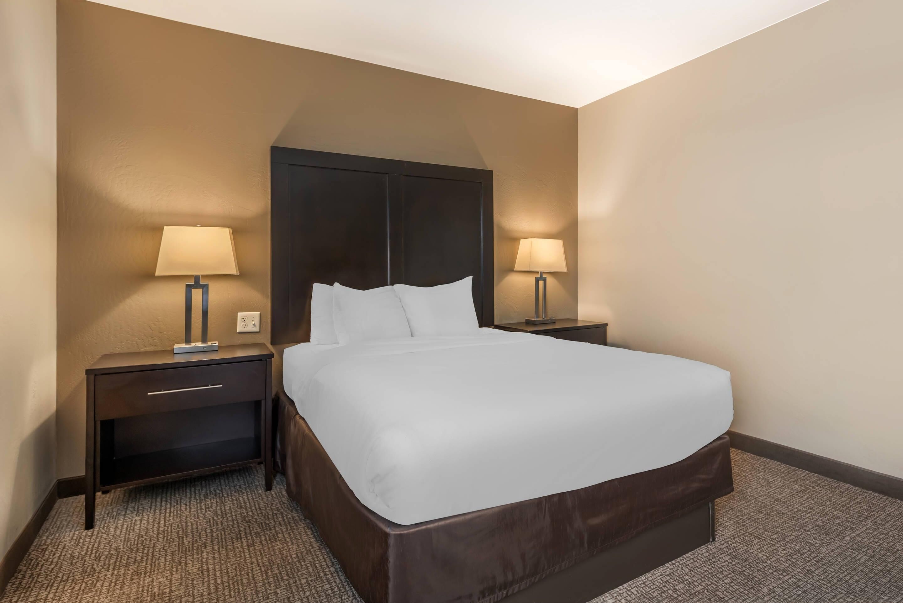 Ein Hotelzimmer mit einem großen Bett, zwei Nachttischen mit Lampen und einem Teppichboden.