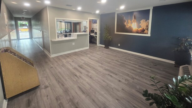 Une pièce spacieuse avec un plancher en bois, un comptoir d’accueil, un grand tableau représentant le lancement d’une fusée et une plante en pot.