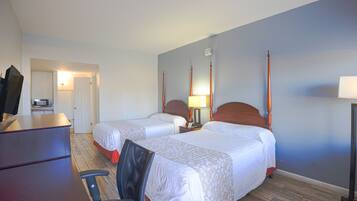Une chambre d’hôtel avec deux lits, un bureau, une chaise, une lampe et un téléviseur.