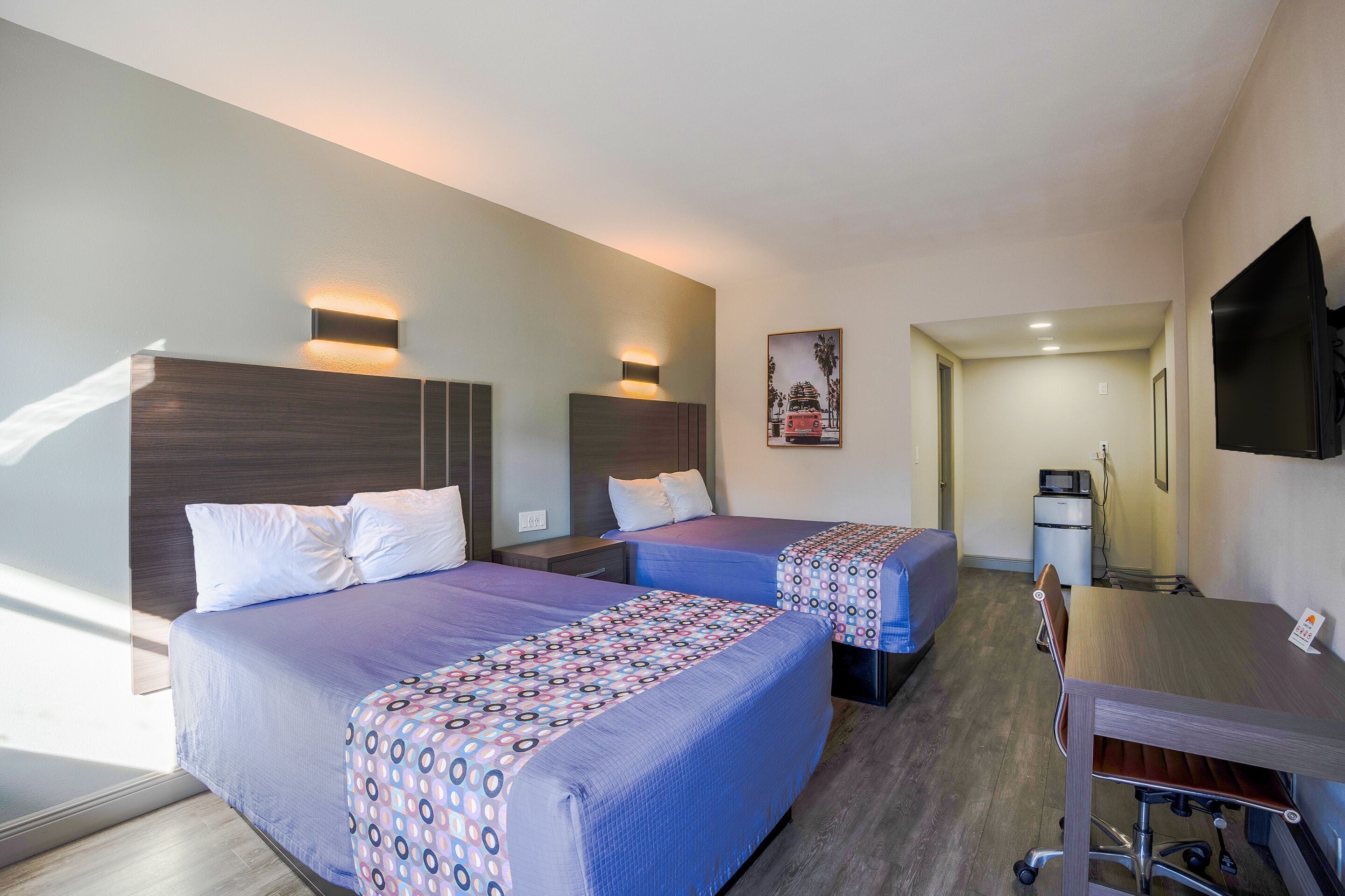 Quarto de hotel com duas camas, uma escrivaninha, uma cadeira, uma televisão e um micro-ondas.