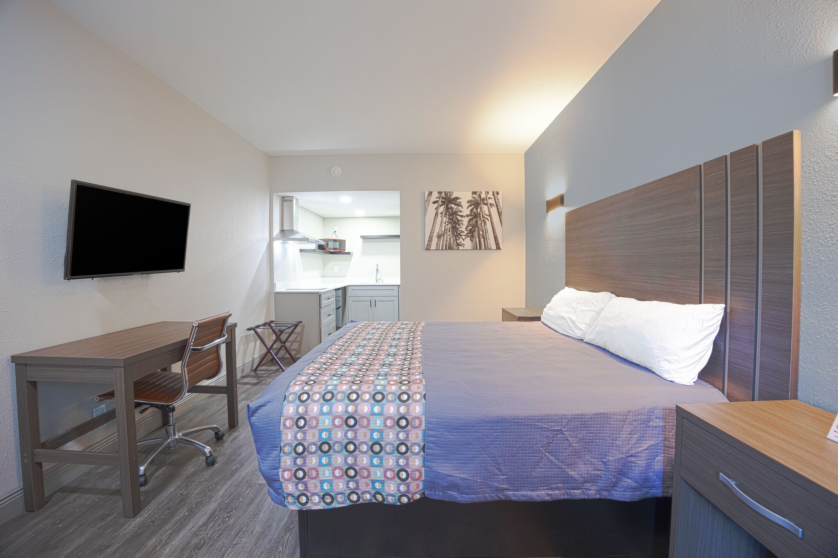 Une chambre d’hôtel avec un lit, un bureau, une chaise, une télévision et, au fond, une petite cuisine.
