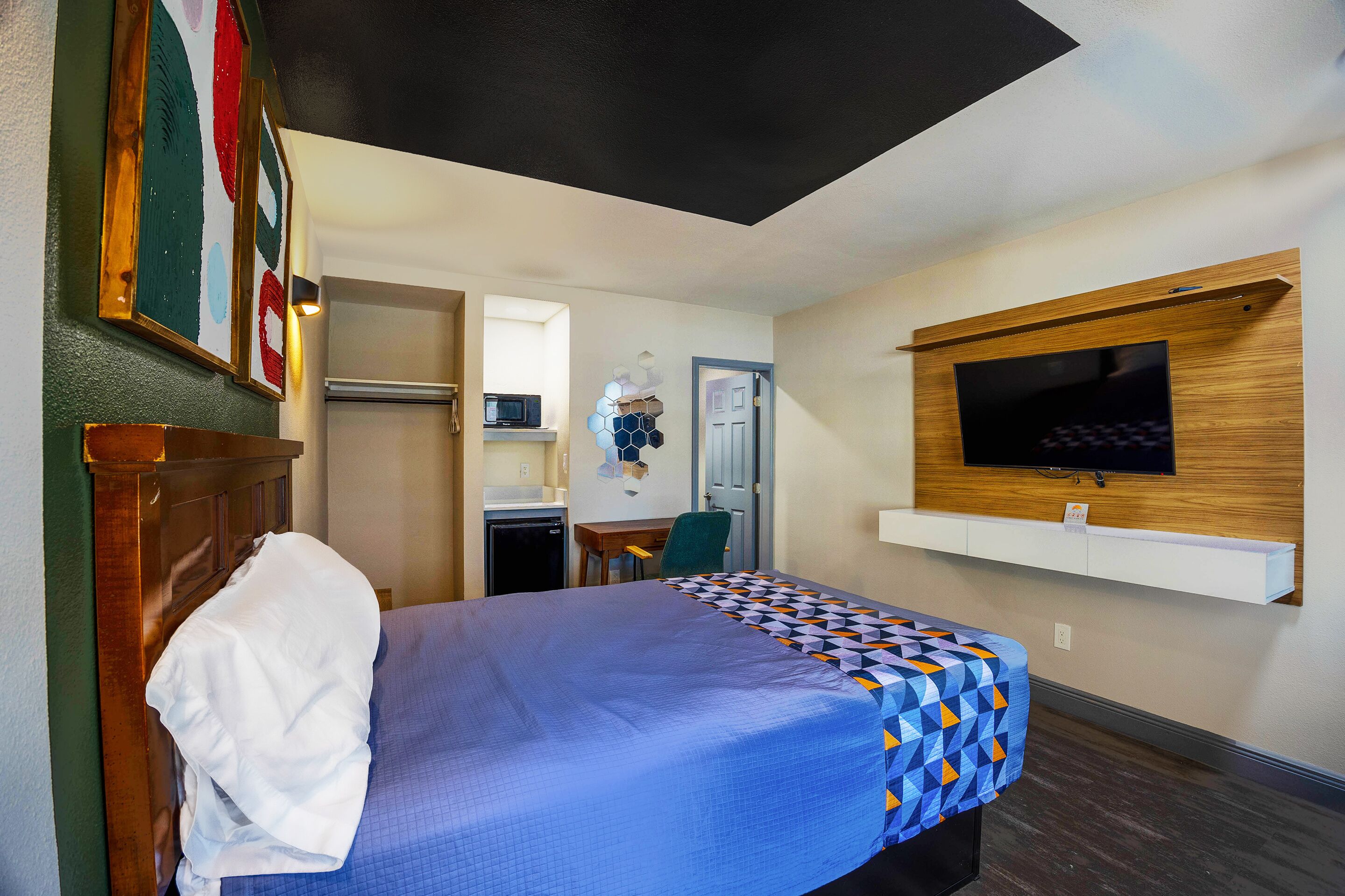 A hotel room with a bed, a TV mounted on the wall, a desk with a chair, and a microwave.