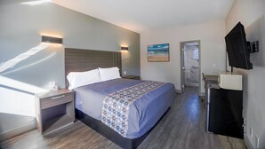 Une chambre d’hôtel moderne avec un grand lit, des tables de chevet, un téléviseur à écran plat et une vue sur la plage, accessible par une porte ouverte.