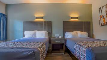 A hotel room with two beds, each with a headboard and bedside tables. There is a small table between the beds with a lamp and a phone.