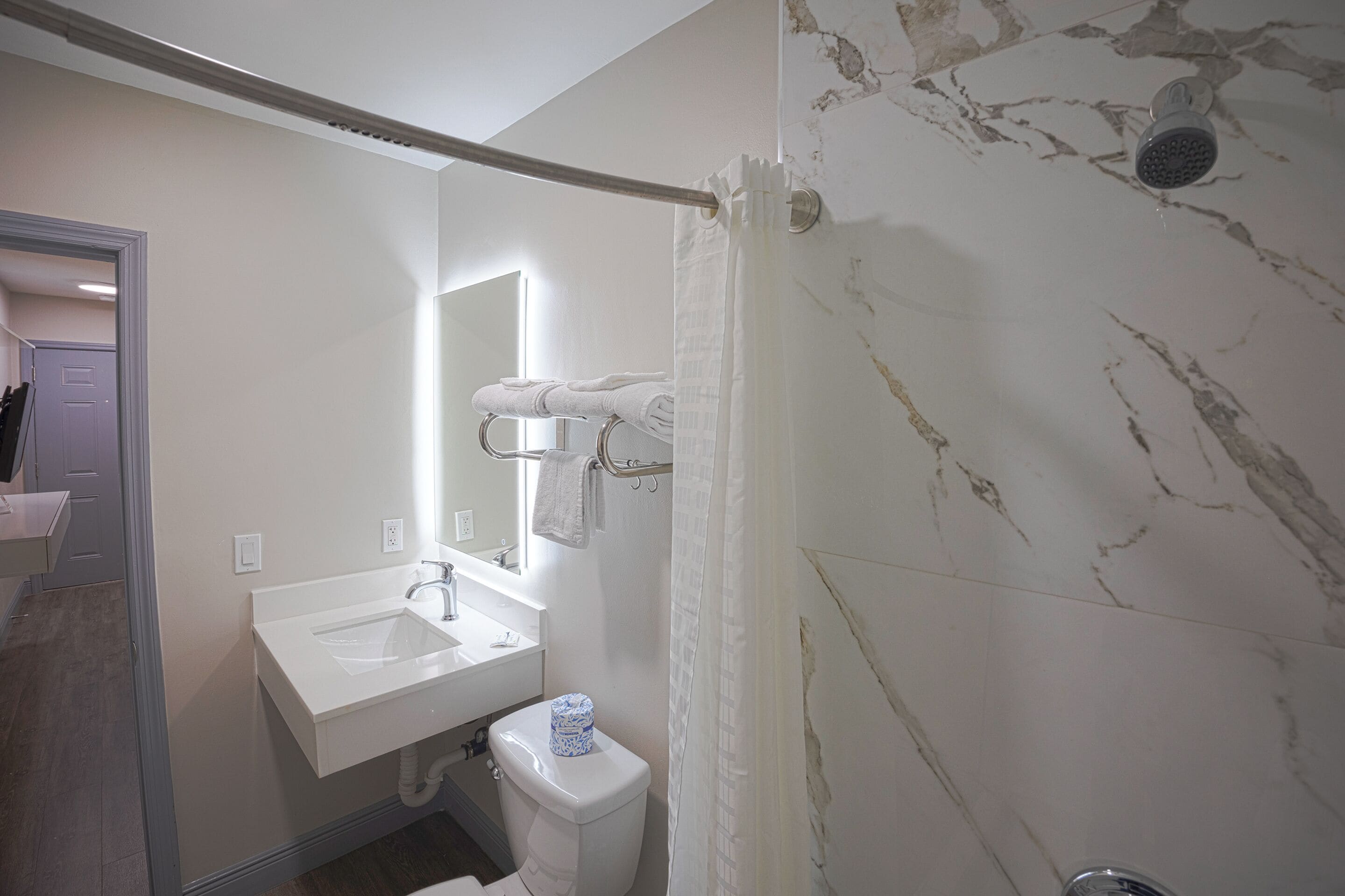 A bathroom with a marble wall, a white sink, a toilet, and a shower curtain.