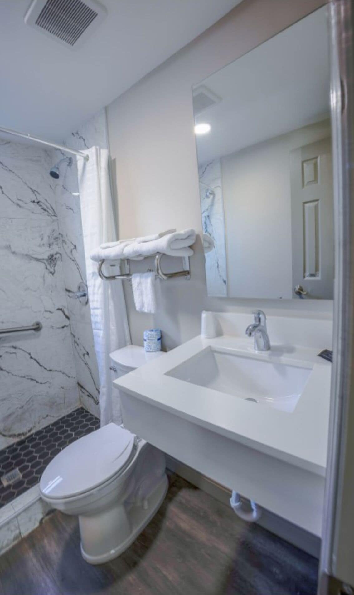 A modern bathroom with a marble shower wall, a white sink, and a toilet.