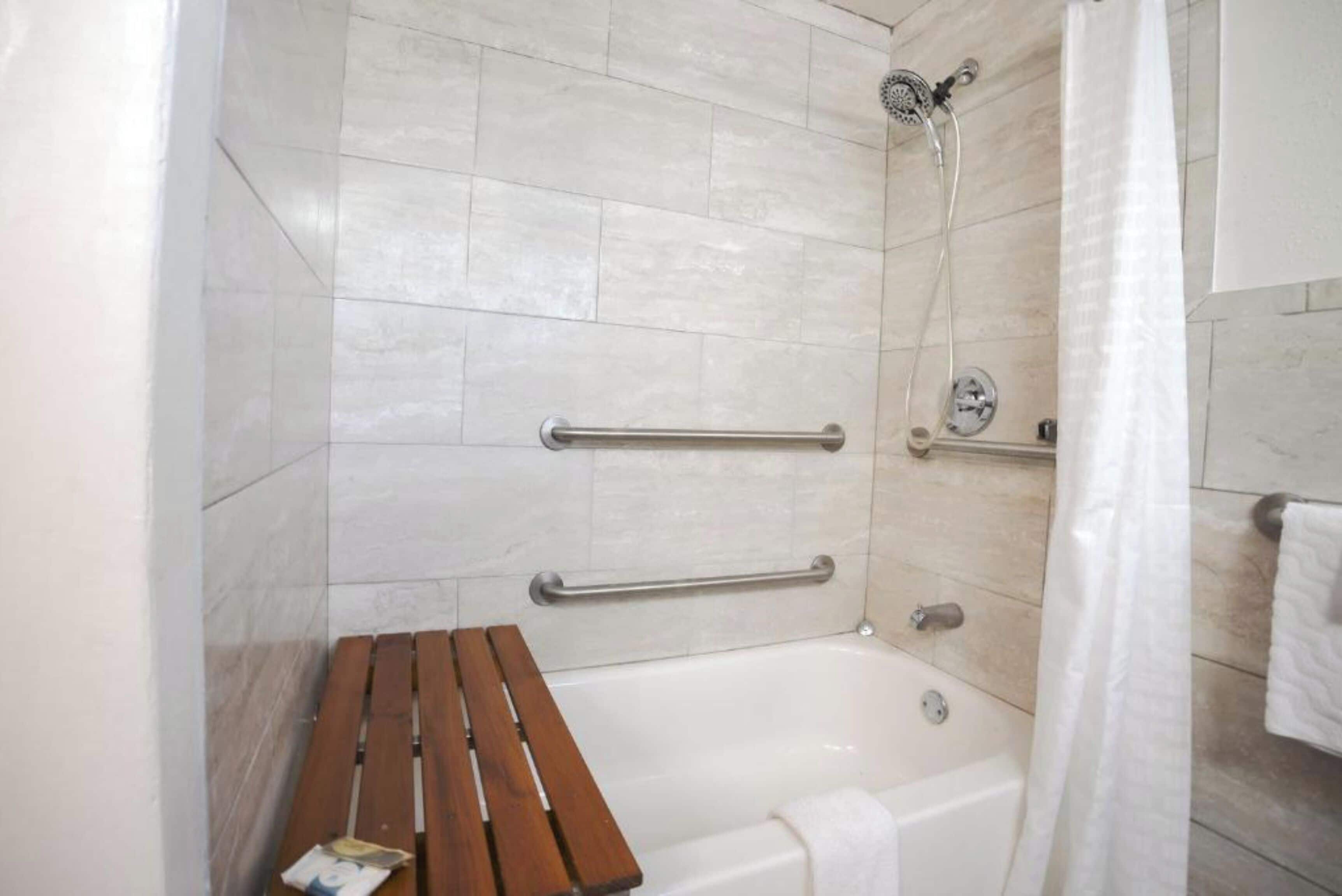 Un baño con una bañera, un banco de madera y dos barras de apoyo.