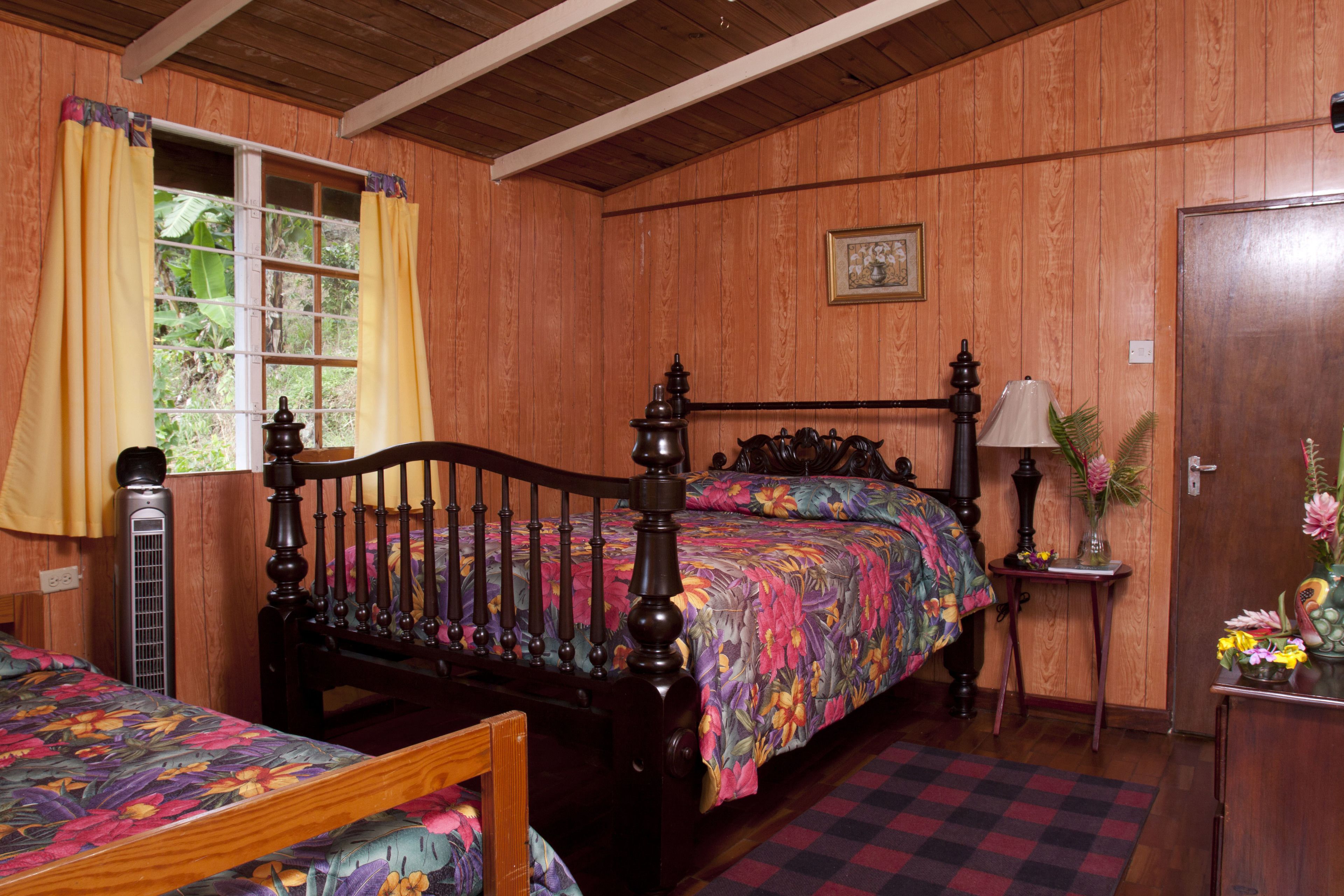Une chambre à coucher aux murs lambrissés, avec un lit, une table de chevet dotée d’une lampe et une fenêtre avec des rideaux.