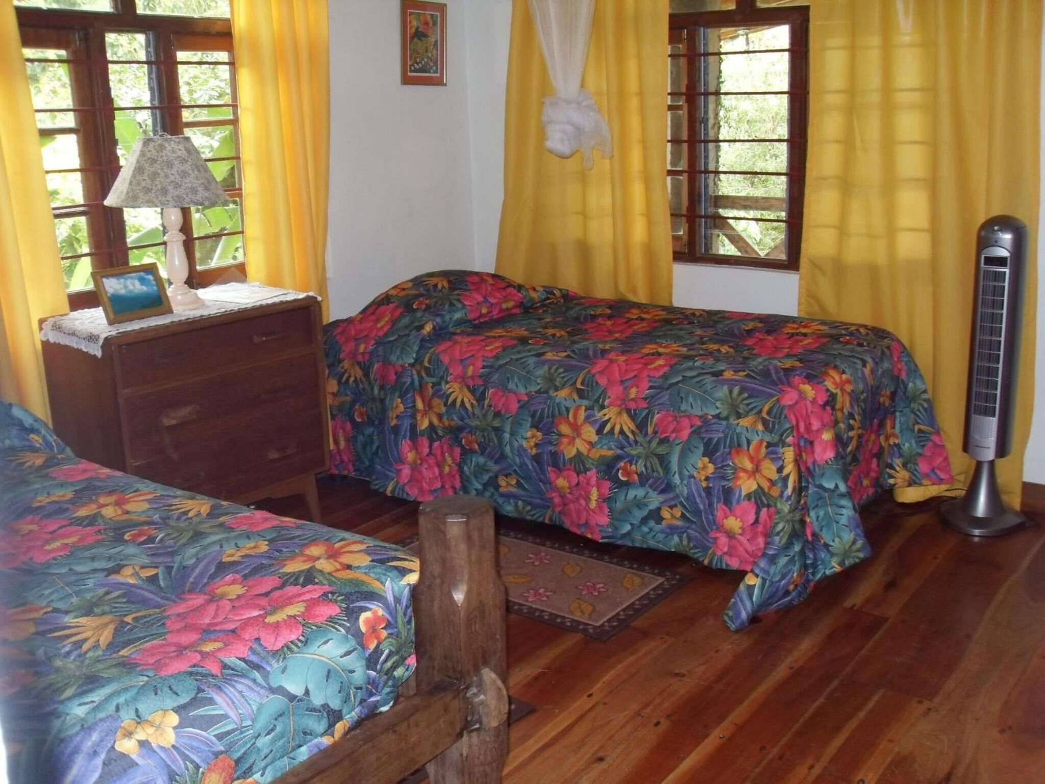 Una habitación con dos camas, un aparador de madera, una lámpara de noche y un calefactor.