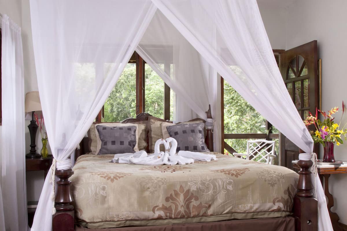 A four-poster canopy bed with a floral bedspread, wooden headboard, and a nightstand with a lamp.