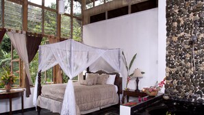 A bedroom with a four-poster bed, a stone wall, a small pond, and a view of greenery. - Forres Park Resort & Spa (Mavis Bank)