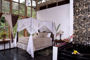 Un dormitorio con cama con dosel, pared de piedra, un pequeño estanque y vistas a la vegetación.