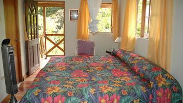 Un dormitorio con colcha estampada, puerta de madera, ventana con cortinas y una mesita de noche.