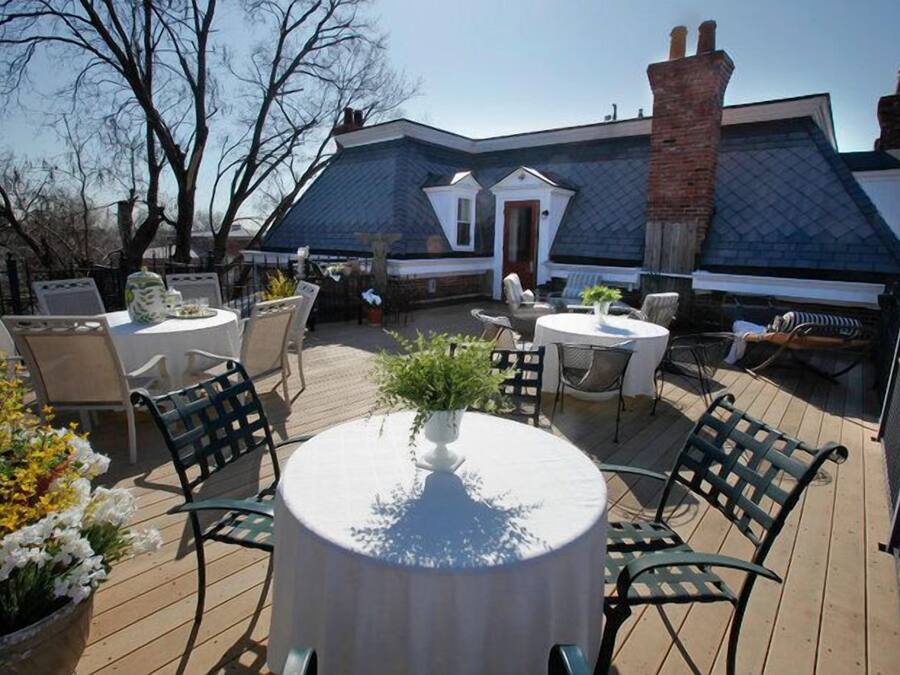 An outdoor patio area with round tables and chairs, surrounded by potted plants and a brick chimney.