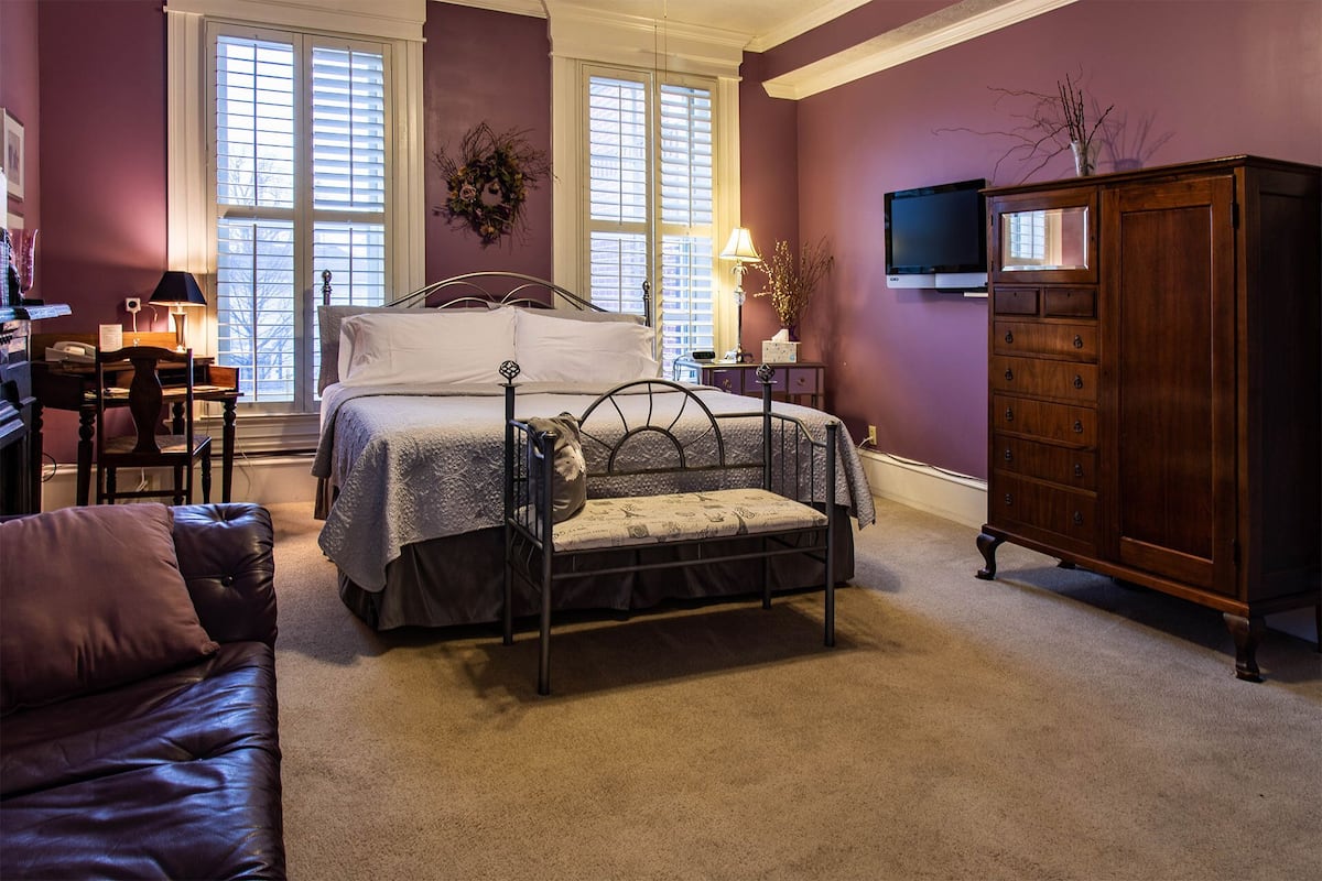A bedroom with a bed, a dresser, a television, and a desk with a lamp.